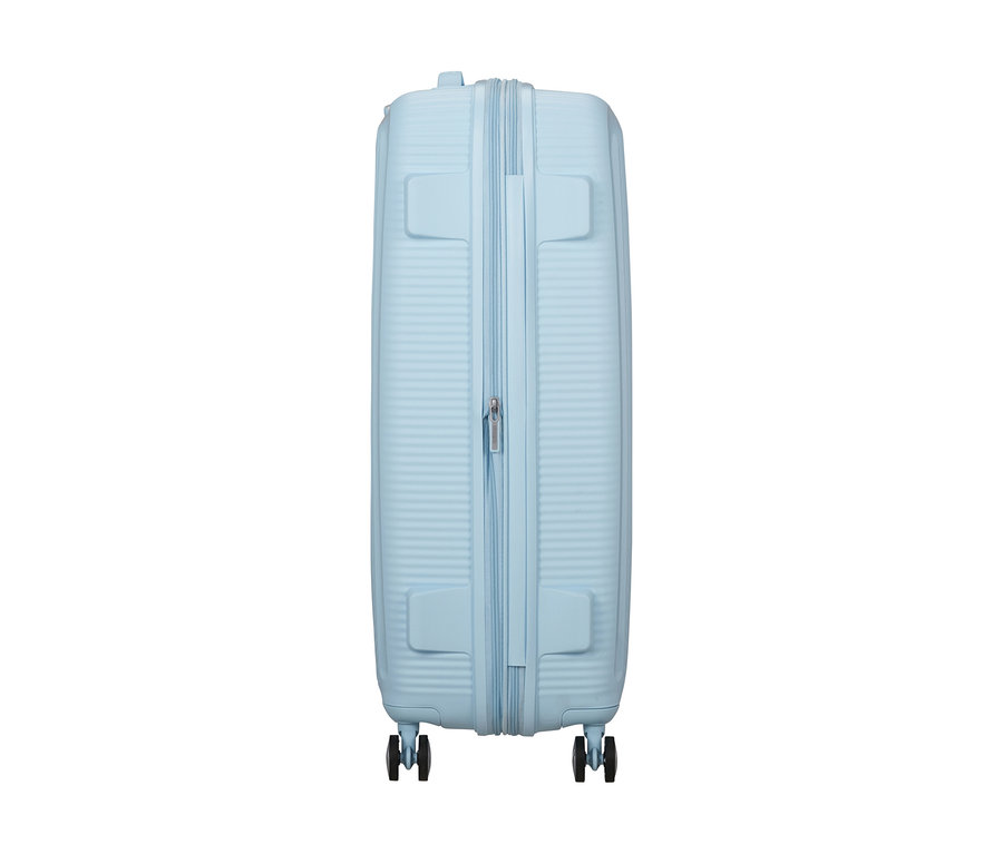 Großer American Tourister Soundbox Hartschalen-Koffer in Pastellblau, von der Seite gezeigt, mit Reißverschluss und vier Rollen.