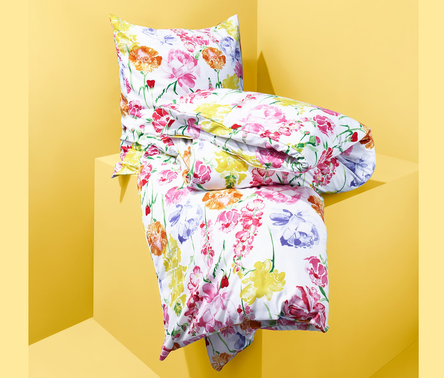 Gefaltete Microfaser-Bettwäsche mit Blumenmuster liegt auf gelbem Sockel.