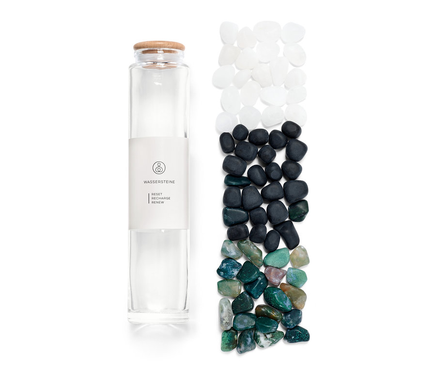 Eine Glasflasche mit Etikett und daneben Wassersteine in Weiss, Schwarz und Grün.