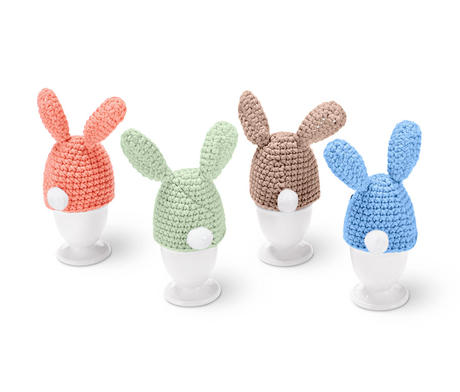 DIY-Häkelset »Eierwärmer« in Form von Hasen in den Farben Aprikose, Grün, Beige und Blau auf weißen Eierbechern.
