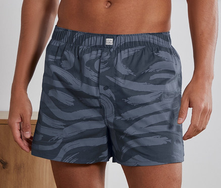 Mann trägt 2 Webboxershorts mit Alloverprint.