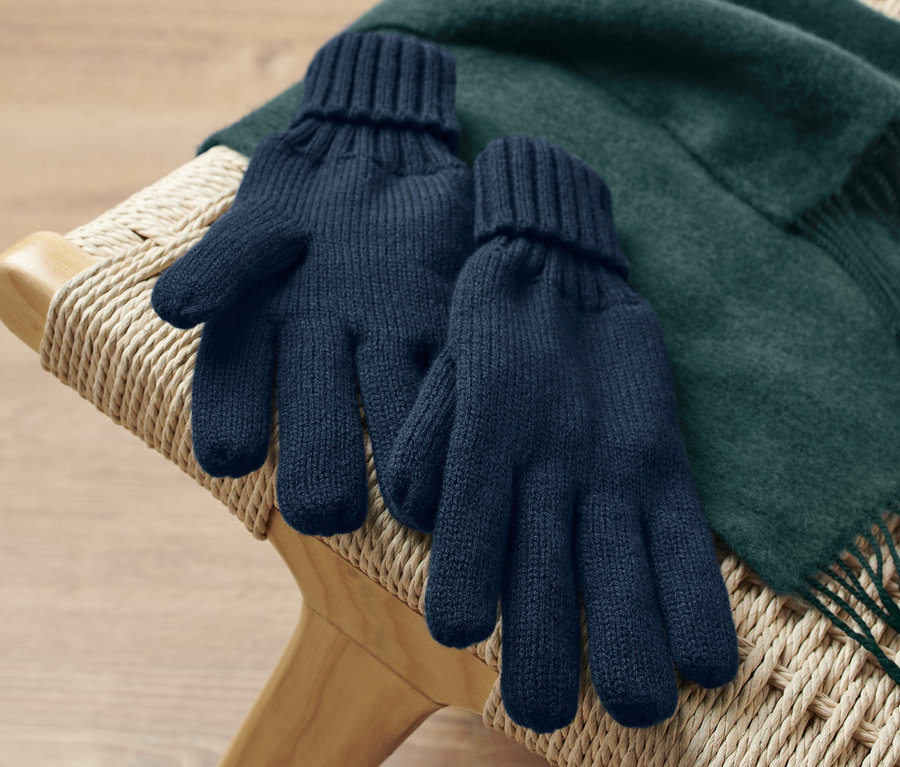 Auf einer Korbliege liegen Strickhandschuhe und ein grüner Schal.