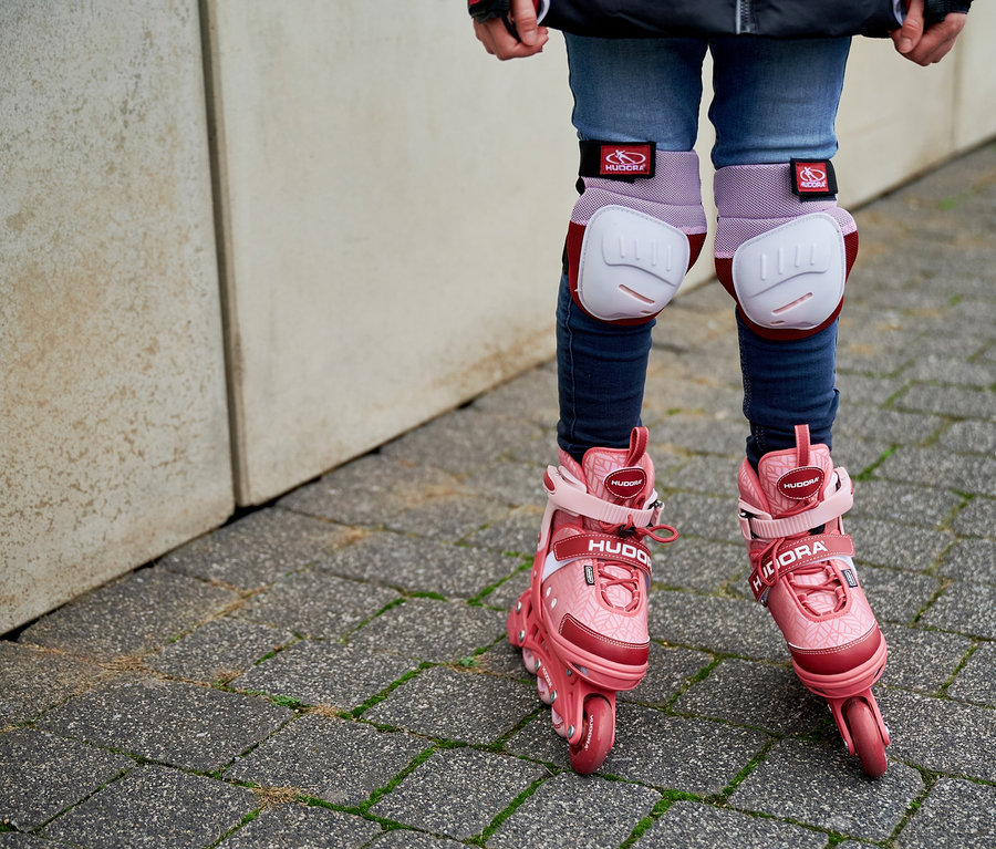 Beine eines Kindes mit HUDORA Inline Skates »Mia 2.0« und Knieschützern auf gepflastertem Weg.