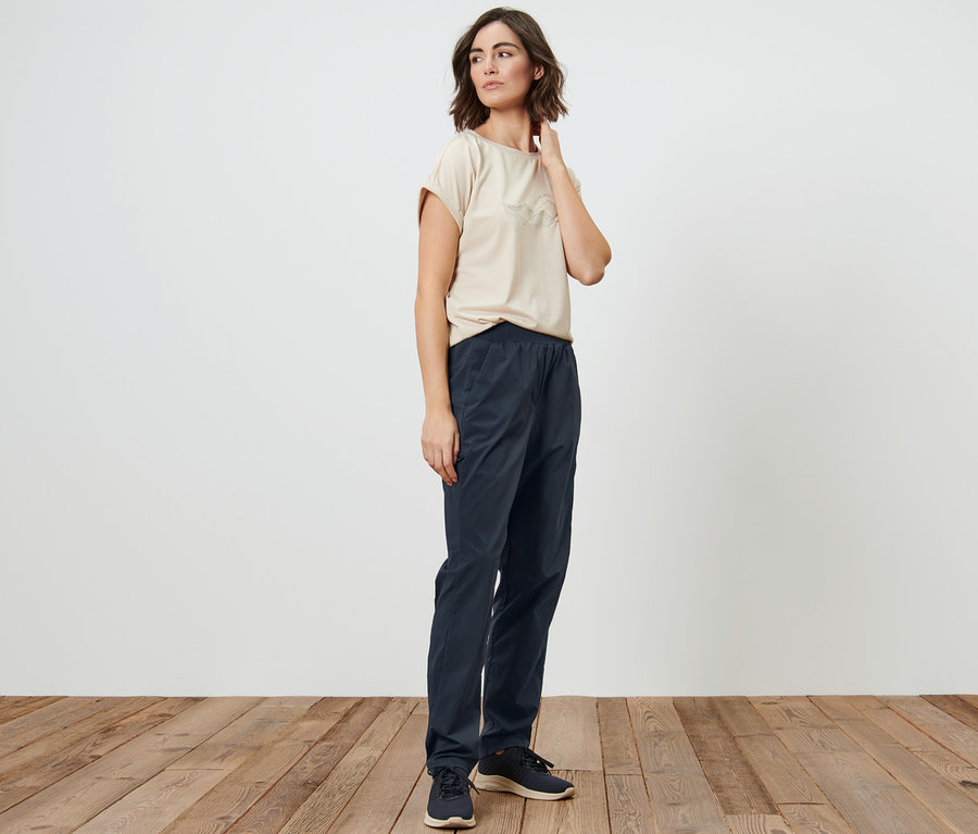 Frau posiert in einem beigen T-Shirt und einer dunkelblauen Funktionswanderhose.
