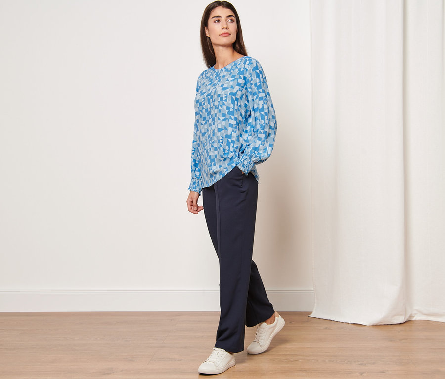 Frau posiert in bedruckter Bluse und marineblauer Hose.