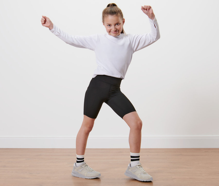 Mädchen in weißem Hemd und 2 Kinder-Sport-Radler steht mit erhobenen Armen.