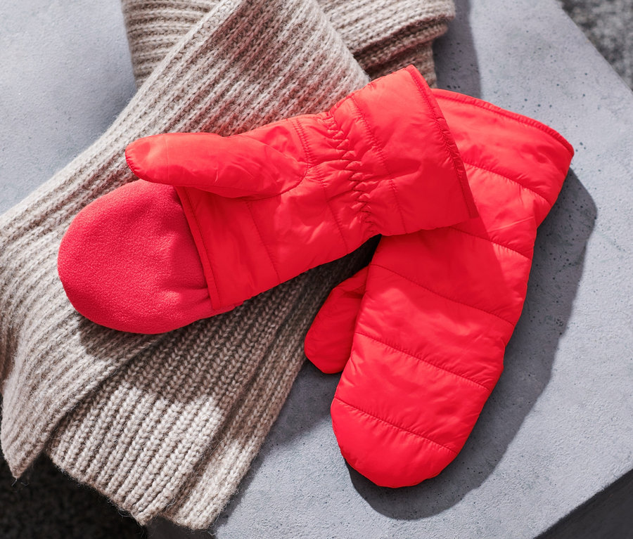 Auf einer grauen Oberfläche liegen rote Stepp-Klappfäustlinge und ein beiger Strickschal.
