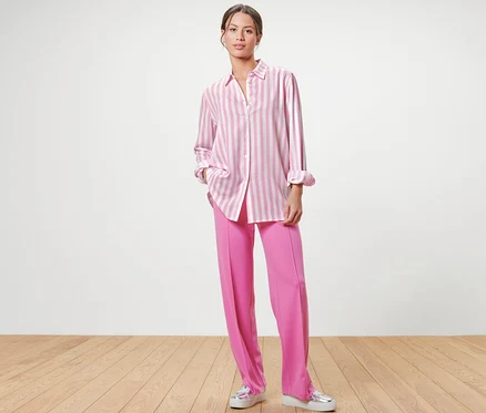 Frau steht und trägt eine rosa Hose und eine gestreifte Bluse, rosa.