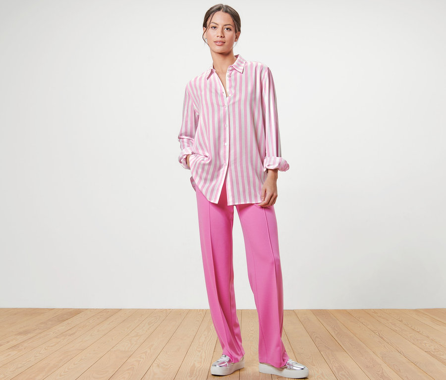 Frau steht und trägt eine rosa Hose und eine gestreifte Bluse, rosa.