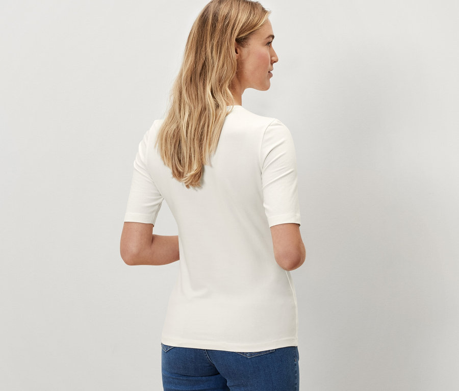 Rückansicht einer Frau in einem cremefarbenen Halbarmshirt und blauen Jeans.