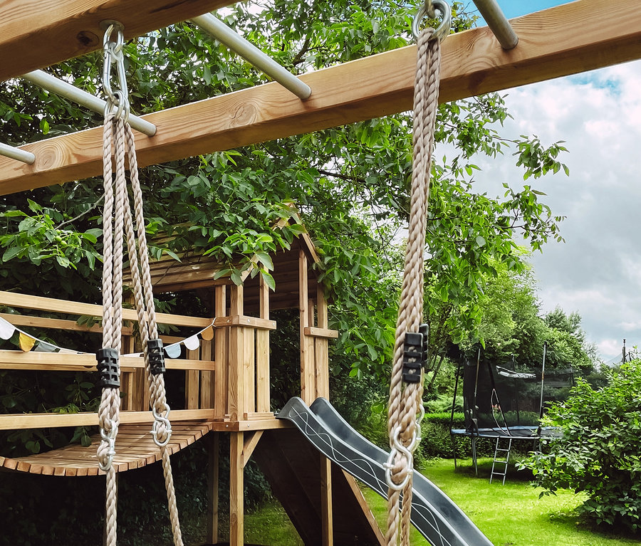 Spielplatz mit Holzrahmen, Rutsche und small foot Skateboard-Schaukel.