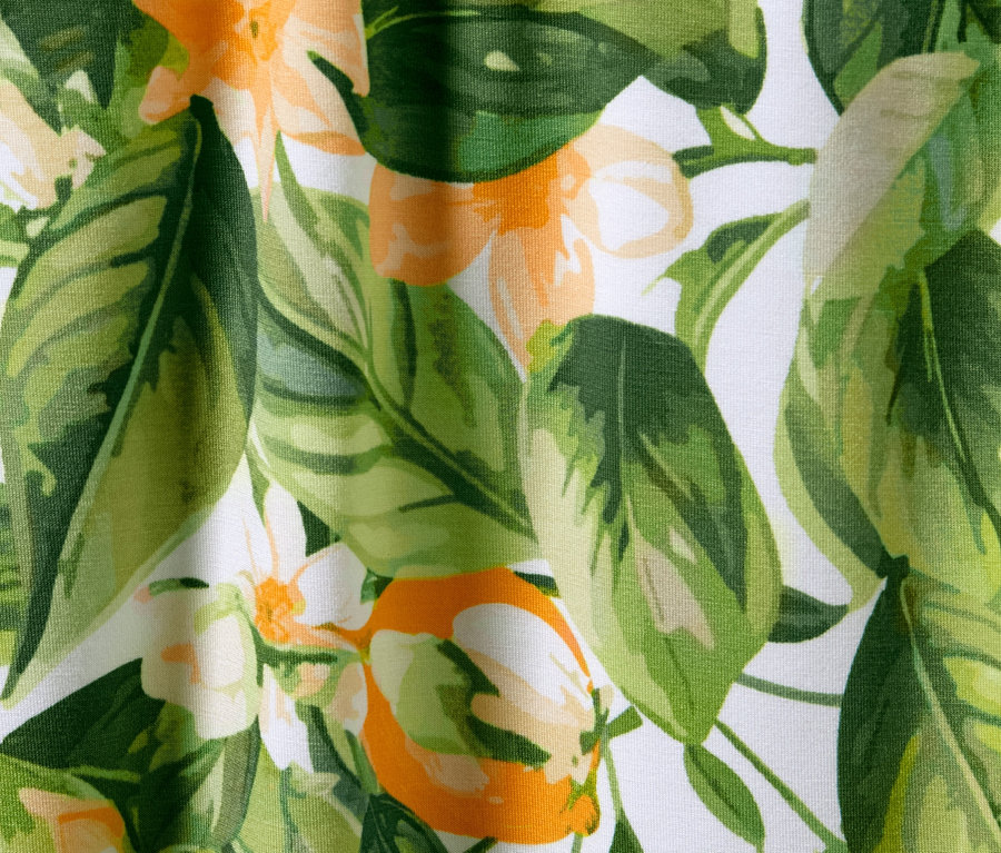 Detailansicht einer bedruckten Palazzohose mit Blättern und Blüten in Grün- und Orangetönen auf weißem Grund.