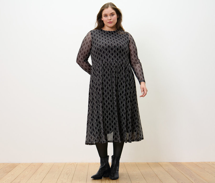 Frau steht und trägt ein bedrucktes Mesh-Kleid.