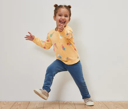 Lächelndes Mädchen springt und trägt eine Kinder-Strickjacke mit Eis-Motiv.