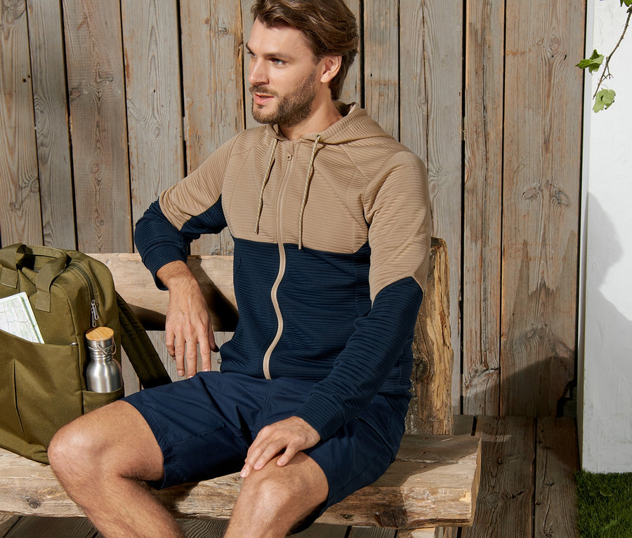 Mann sitzt auf einer Bank und trägt eine Funktionsjacke.