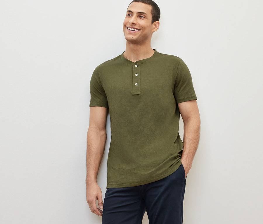 Mann lächelt und posiert in einem khakifarbenen Kurzarm-Henley.