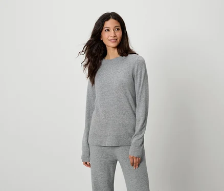 Frau posiert in grauem Pullover und grauer Hose.