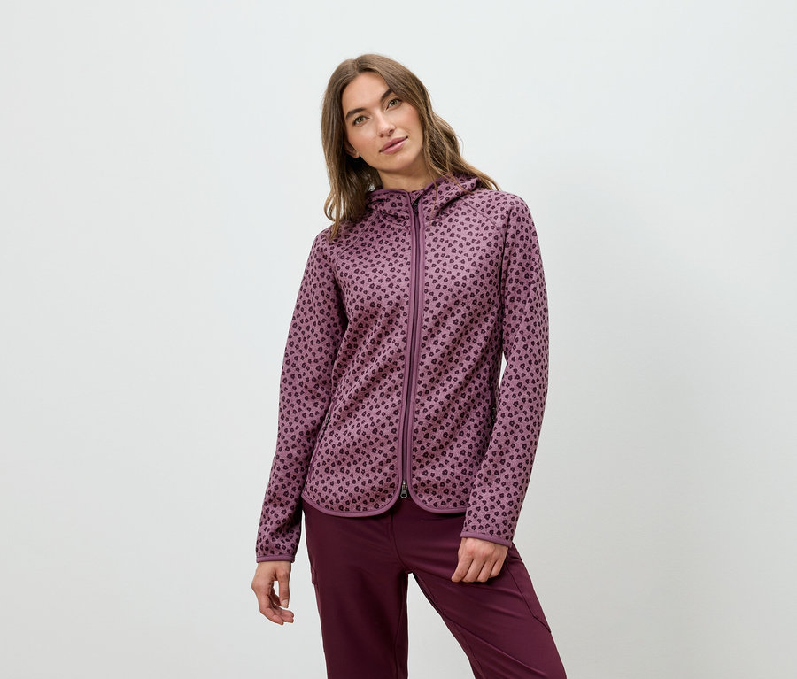 Frau posiert in einem burgunderfarbenen Kapuzenpullover und einer Hose.