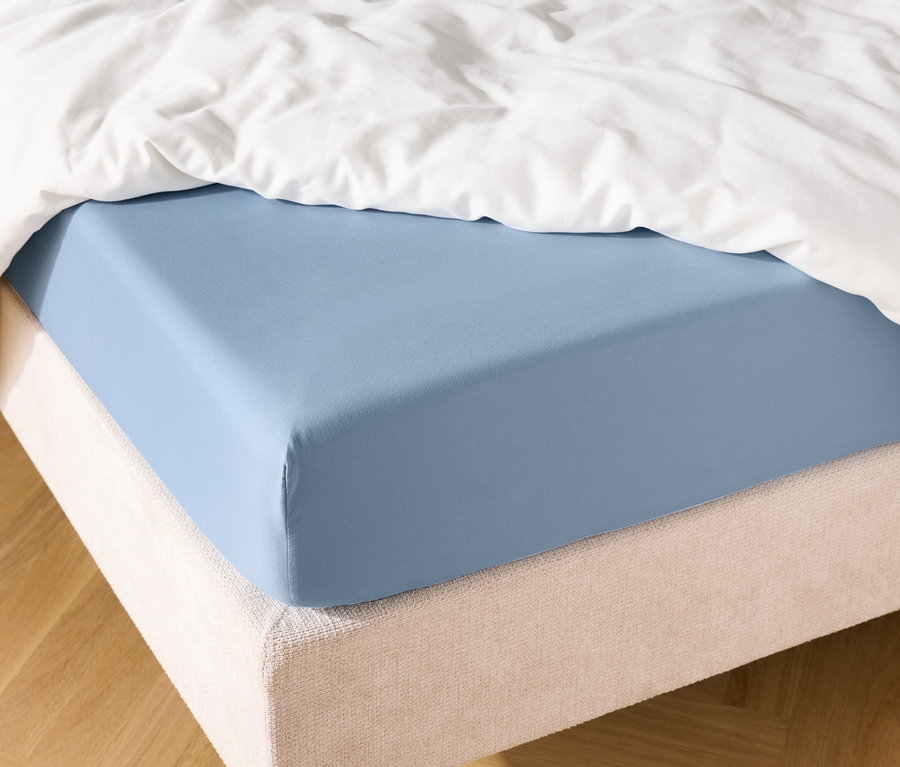Hellblaues Spannbettlaken auf einem Bett mit weißer Bettdecke.