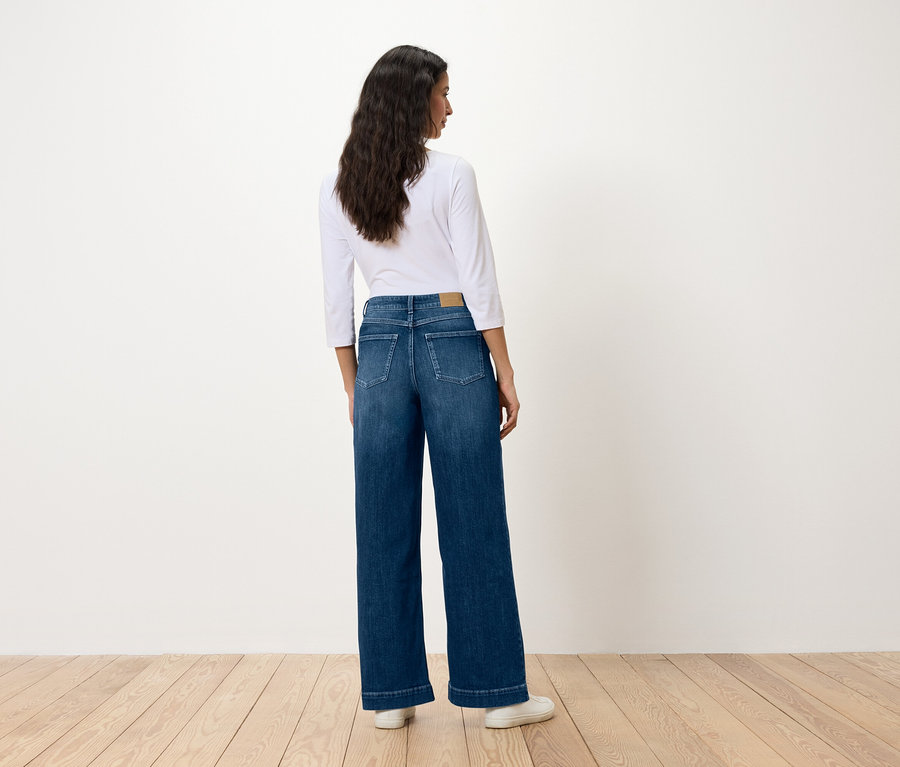 Frau mit dem Rücken zur Kamera trägt blaue, weit geschnittene Jeans und ein weißes Hemd.