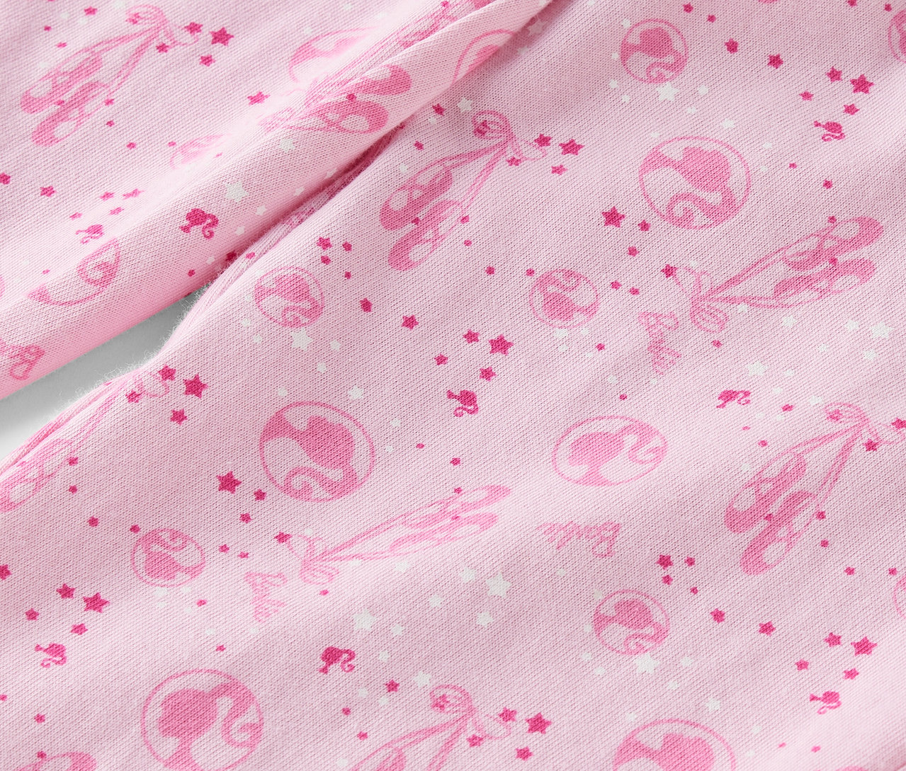 Detailaufnahme eines rosa Stoffes, bedruckt mit Ballettschuhen, Sternen und Barbie-Silhouetten.