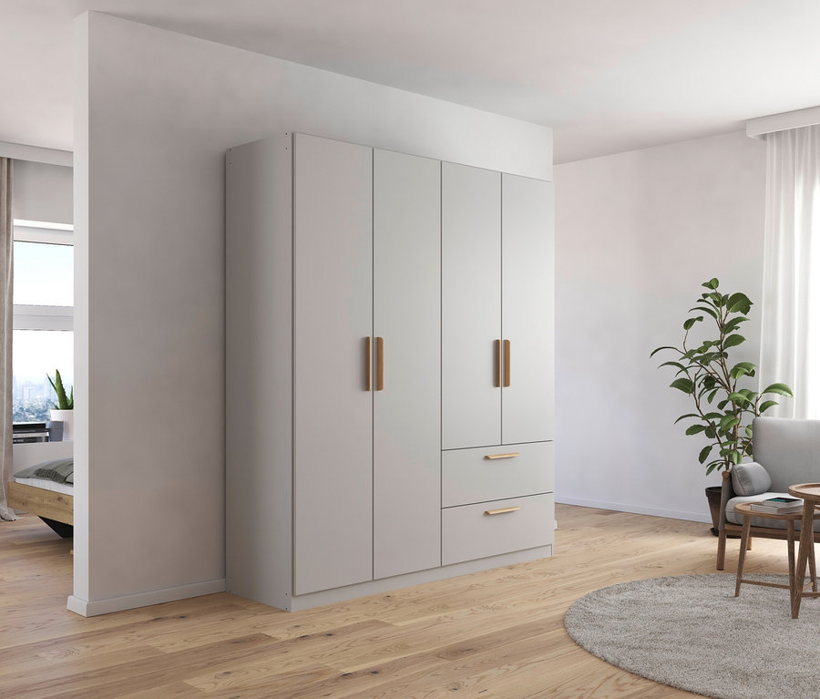 Ein Zimmer mit einem 4-türigen, seidengrauen Drehtürenschrank »Skandi« von Rauch, einem Sessel, einer Pflanze und einem Holzpodest.