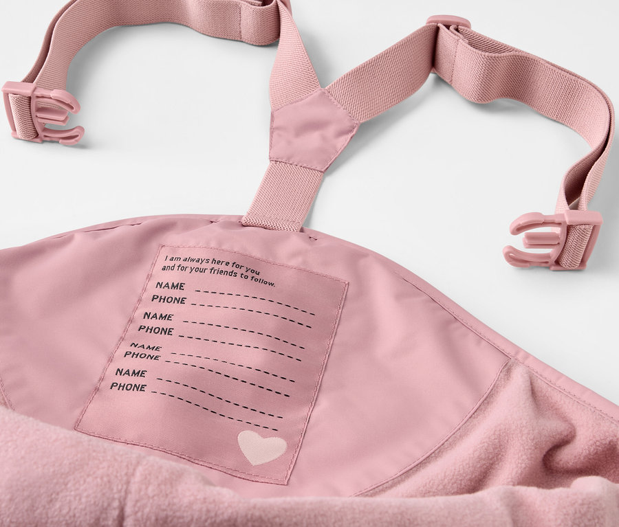 Detail einer rosa Kinder-Thermo-Regenhose mit Latz und Namensschild.