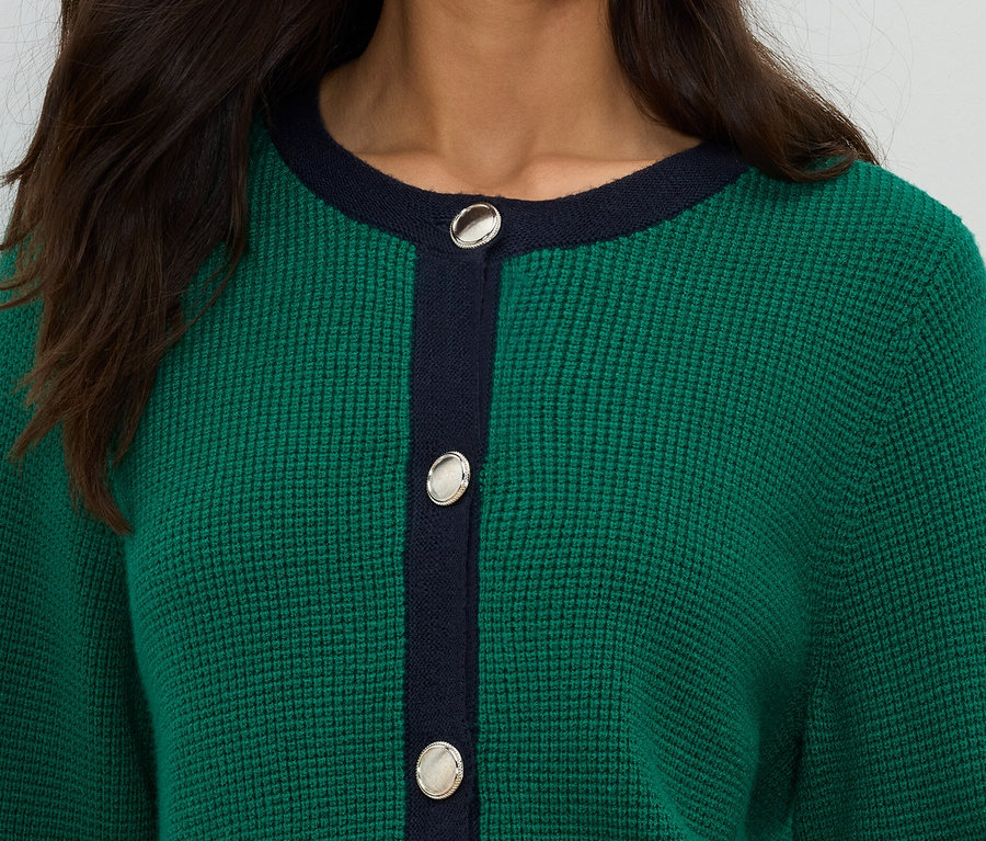 Nahaufnahme einer Frau, die eine grüne Strickjacke mit marineblauen Akzenten und silbernen Knöpfen trägt.