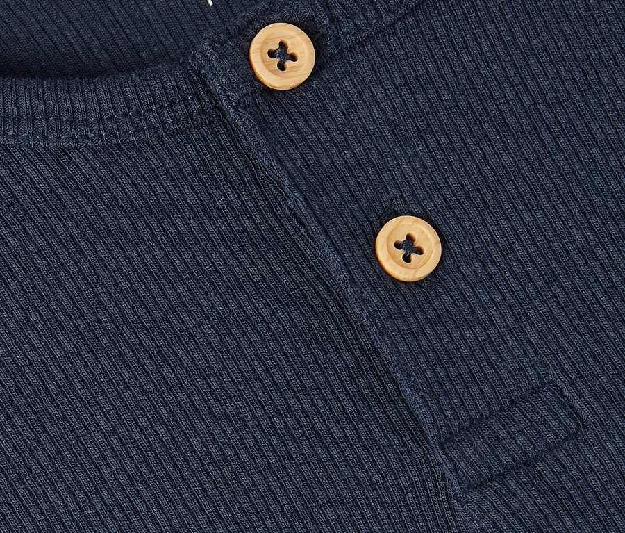Nahaufnahme eines dunkelblauen, gerippten Hemdes mit zwei hellbraunen Knöpfen und dem Namen "name it" in der oberen linken Ecke.