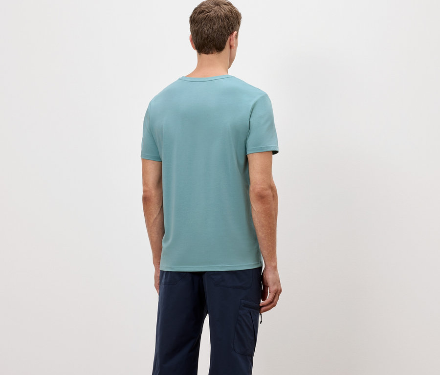 Rückansicht eines Mannes mit hellblauem T-Shirt und dunkelblauer Hose vor einem weißen Hintergrund.