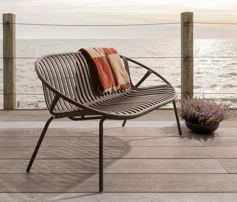 Ein brauner Stuhl mit einer Decke darauf steht auf einer Holzterrasse mit Blick auf das Meer.