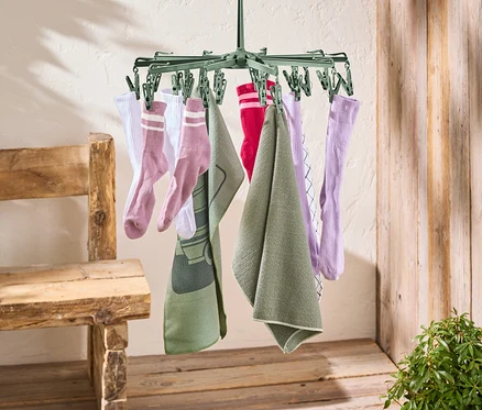 Eine grüne Wäschespinne hängt an einer roten Wäscheleine. An der Wäschespinne hängen Socken und Handtücher.