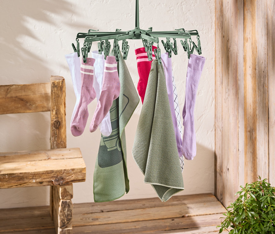 Eine grüne Wäschespinne hängt an einer roten Wäscheleine. An der Wäschespinne hängen Socken und Handtücher.