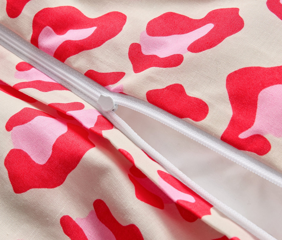 Nahaufnahme eines teilweise geöffneten Reißverschlusses auf einem Stoff mit rosa und roten Flecken.