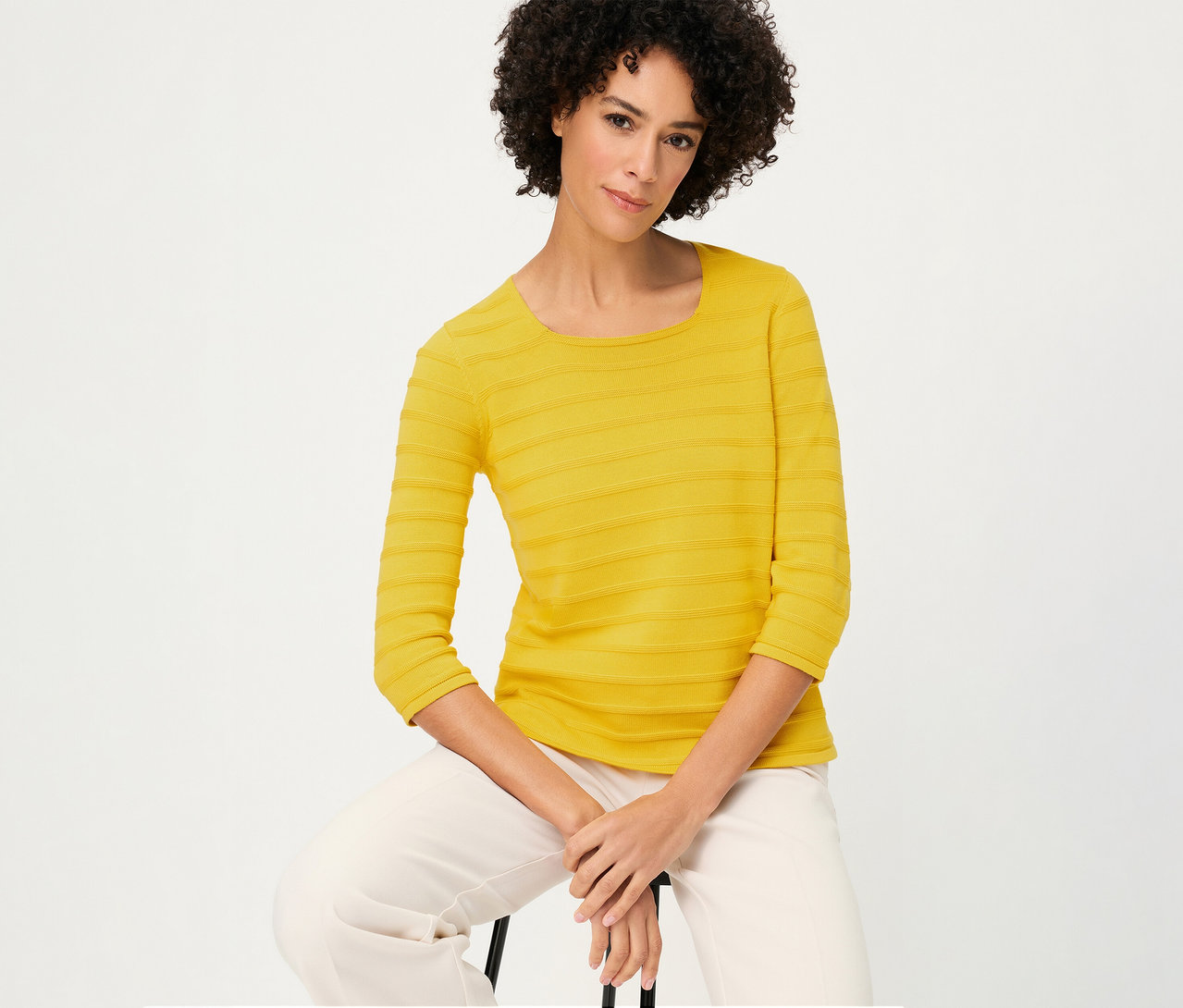 Frau sitzt und trägt einen strukturierten Olsen Pullover mit 3/4-Ärmeln in Gelb und eine helle Hose.
