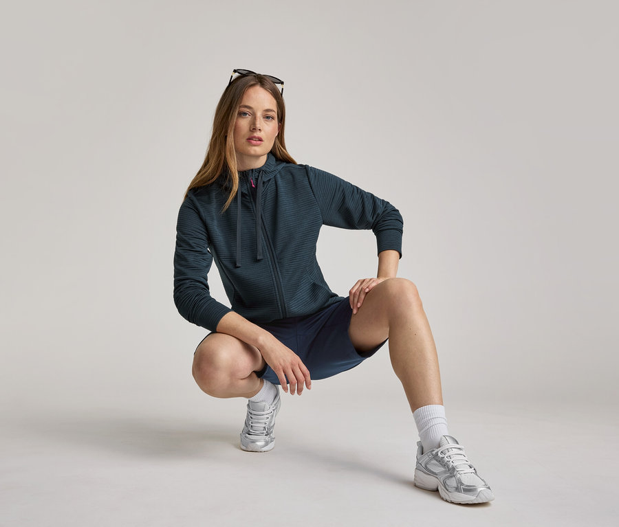 Frau hockt in marineblauer Kapuzenjacke und Shorts. Die Kapuzenjacke ist navy.