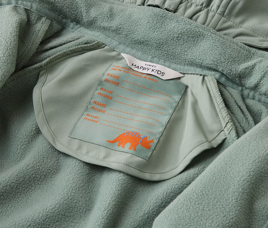 Innenansicht einer hellgrünen Tchibo Happy Kids Jacke mit Namensschild und Triceratops-Motiv.