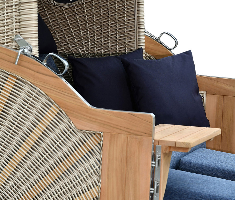Nahaufnahme eines Strandkorbs mit blauem Kissen und ausklappbarem Tisch.