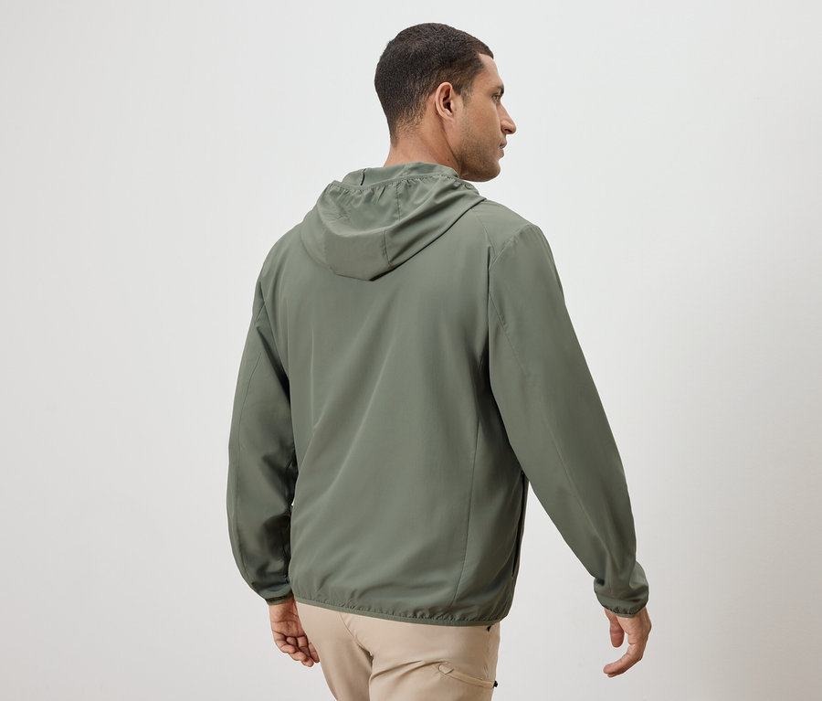 Mann von hinten, trägt eine olivgrüne Jacke mit Kapuze und beigefarbene Hosen.