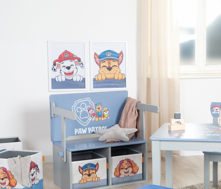 Zwei Paw Patrol-Poster hängen über einer blauen Kinderbank mit Paw Patrol-Motiven, unter der sich zwei Aufbewahrungsboxen befinden. Rechts befindet sich ein Tisch mit Stuhl und Bauklötzen.