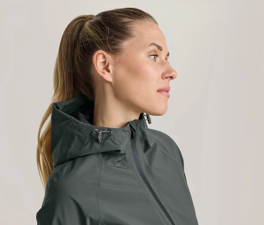 Frau im Profil, die eine dunkelgrüne Kapuzenjacke trägt und nach rechts blickt. Ihr Haar ist zu einem Pferdeschwanz gebunden.
