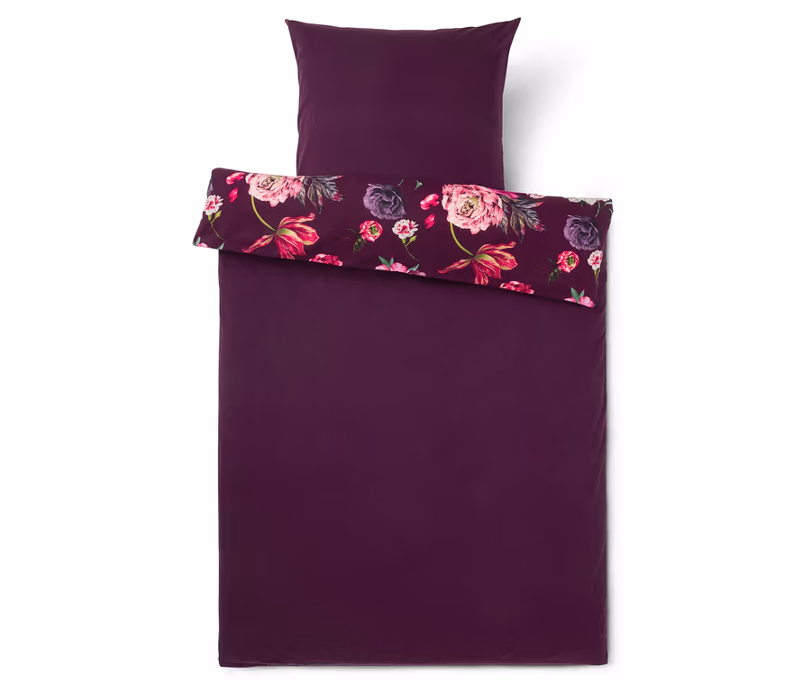 Dunkelviolette Bettwäschegarnitur mit Kissenbezug, der Bettbezug ist umgeschlagen und zeigt ein Blumenmuster mit rosa und violetten Blüten.