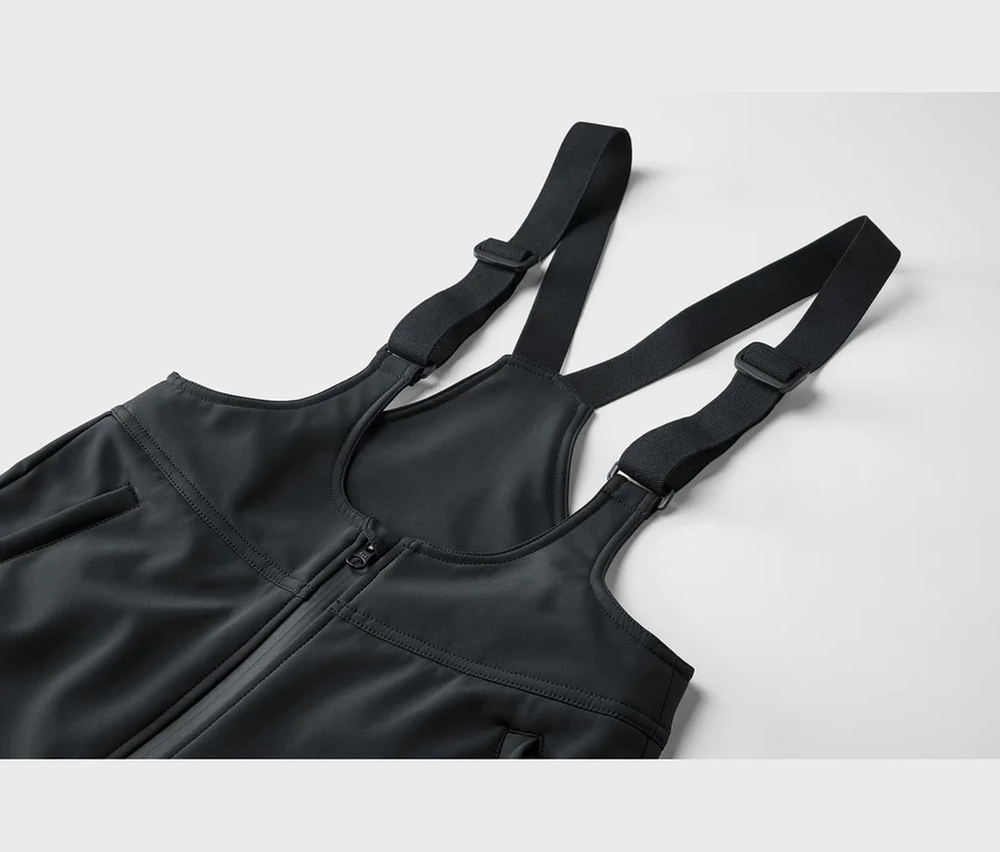 Nahaufnahme des oberen Teils einer schwarzen Latzhose mit verstellbaren Schulterträgern und einem Reißverschluss vorne.