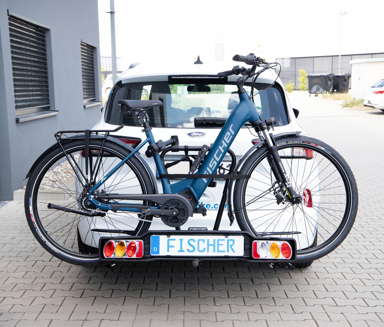 Weißes Auto mit schwarzem Kupplungs-Fahrradträger SmartLine black, der ein blaues Fischer E-Bike transportiert.