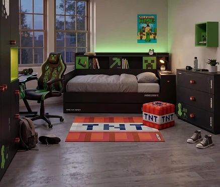 Ein Minecraft-Jugendzimmer mit einem dunklen Roba Jugendbett »Minecraft« mit integrierten Regalen und Motiven. Ein grüner Gaming-Stuhl, ein Schreibtisch und ein Kleiderschrank mit TNT-Griffen stehen im Raum. Auf dem Boden liegen ein TNT-Teppich und ein TNT-Hocker.