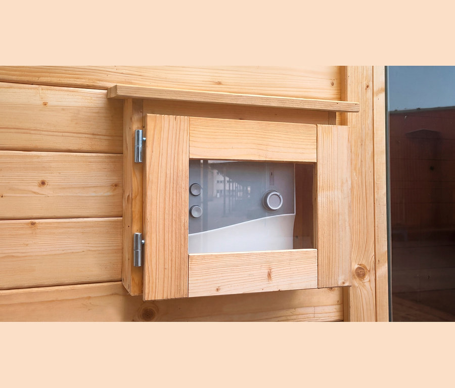 Nahaufnahme einer hellen Holzwand mit einem offenen Holzrahmen, der ein grau-weißes Bedienfeld mit zwei Knöpfen und einem Drehregler zeigt, befestigt mit silbernen Scharnieren.