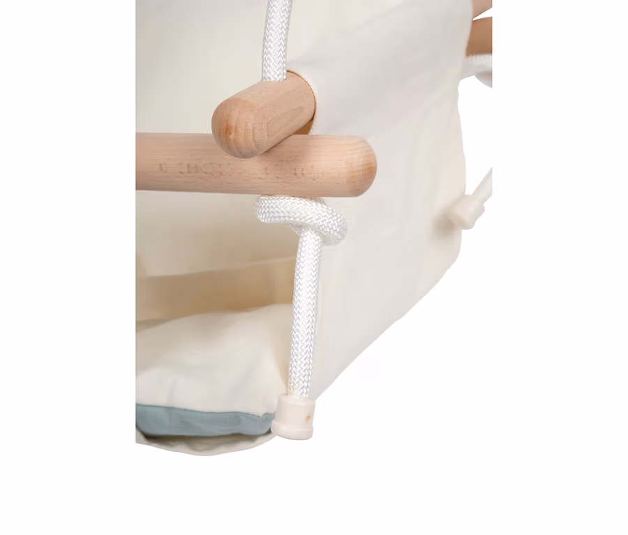 Nahaufnahme der small foot Babyschaukel Komfort, die den cremefarbenen Stoffbezug, helle Holzstangen und weiße geflochtene Seile zeigt. Ein hellblaues Kissen ist am Boden des Sitzes sichtbar.