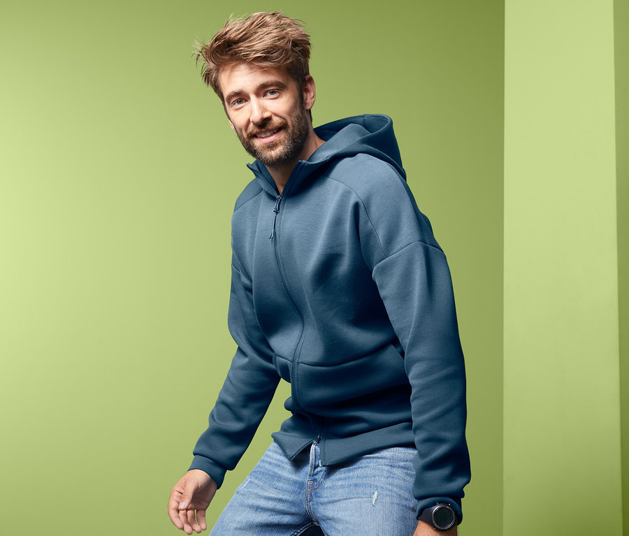 Mann posiert in blauer Funktionsjacke mit Kapuze und Jeans.