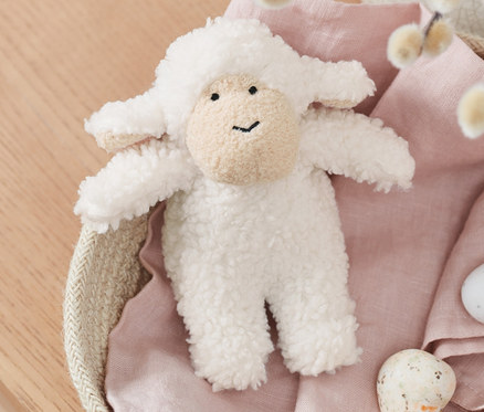 Ein Schaf mit Sound liegt in einem Korb mit Weidenkätzchen und bemalten Eiern.