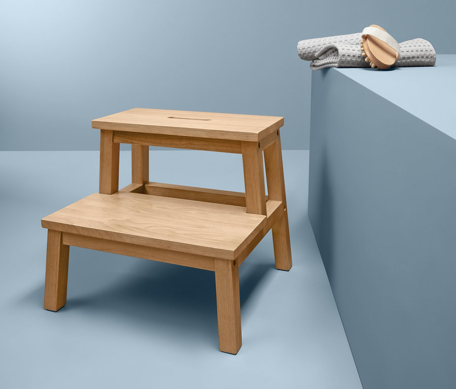 Ein Tritthocker aus Rubberwood steht neben einem grauen Handtuch und einer Bürste auf blauem Hintergrund.